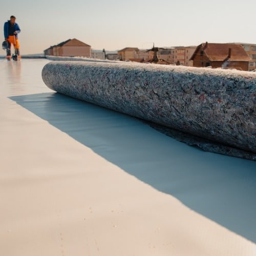 Roofer installs roll of TPO roofing.